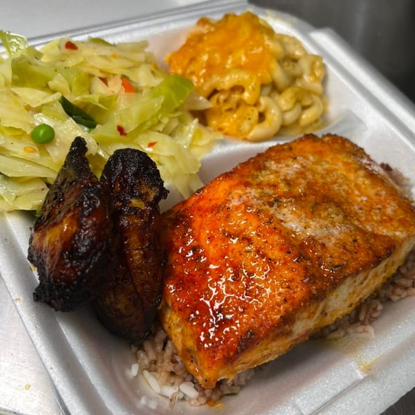 Soul food meal with grilled salmon, rice, dark chicken, macaroni and cheese, and cabbage.