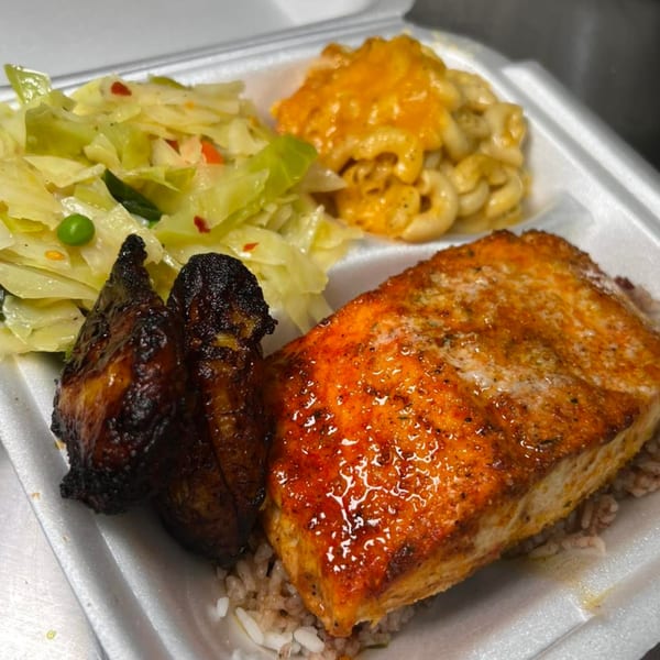A soul food meal with salmon, two chicken drumsticks, cabbage, and macaroni and cheese.