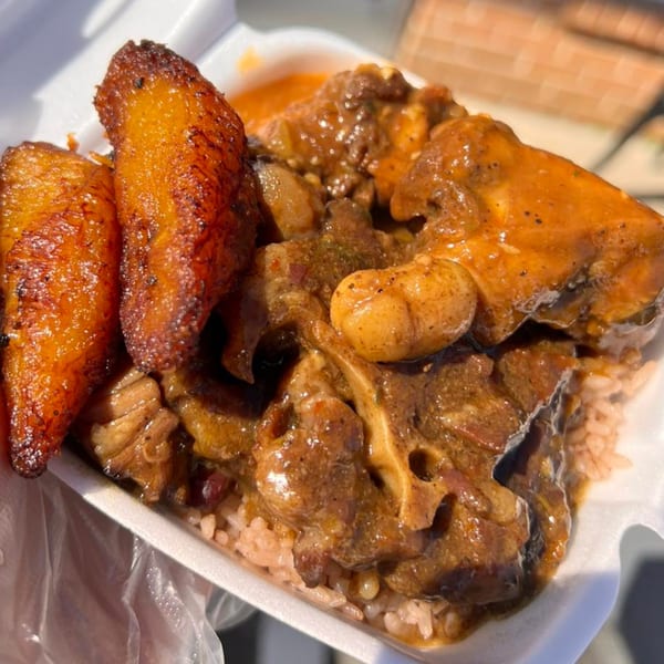 A close-up of a soul food meal with oxtail, rice, and fried plantains in a takeout container.