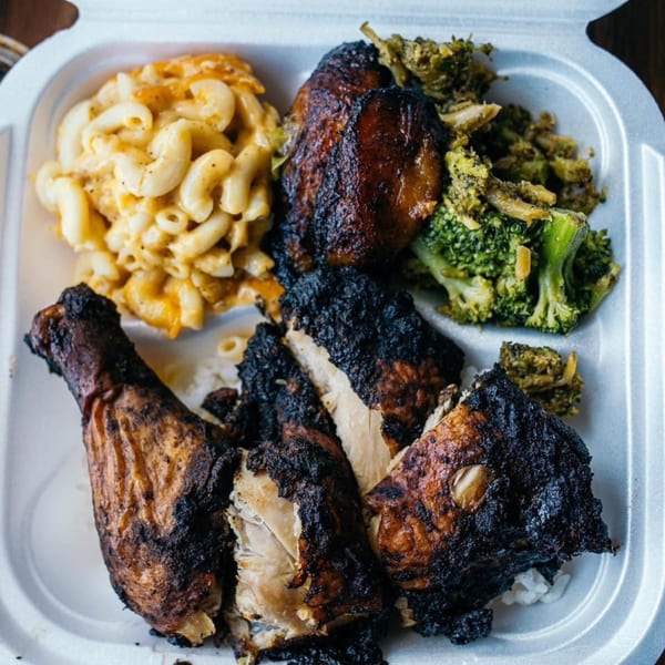 Soul food meal with dark grilled chicken, macaroni and cheese, and broccoli in a takeout container.