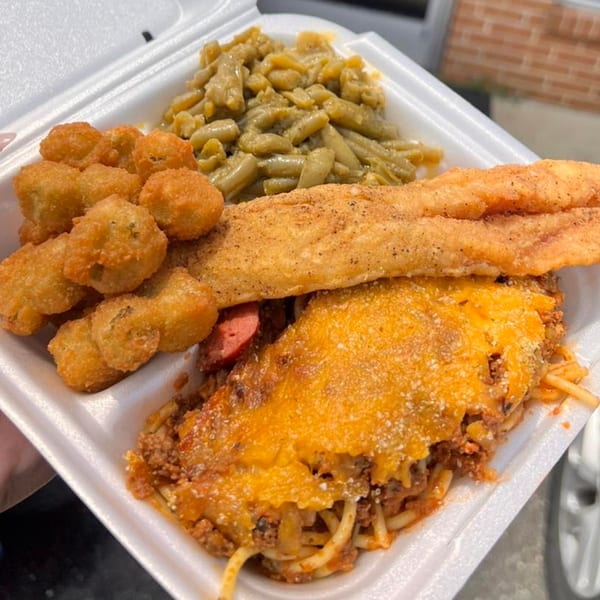 Soul food platter with fried fish, baked spaghetti, fried okra, and green beans in a to-go container.