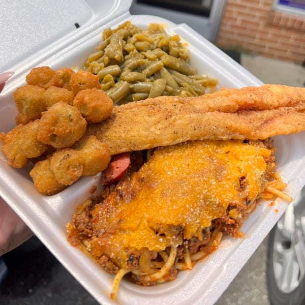 Soul food platter with fried fish, baked spaghetti, fried okra, and green beans in a takeout container.